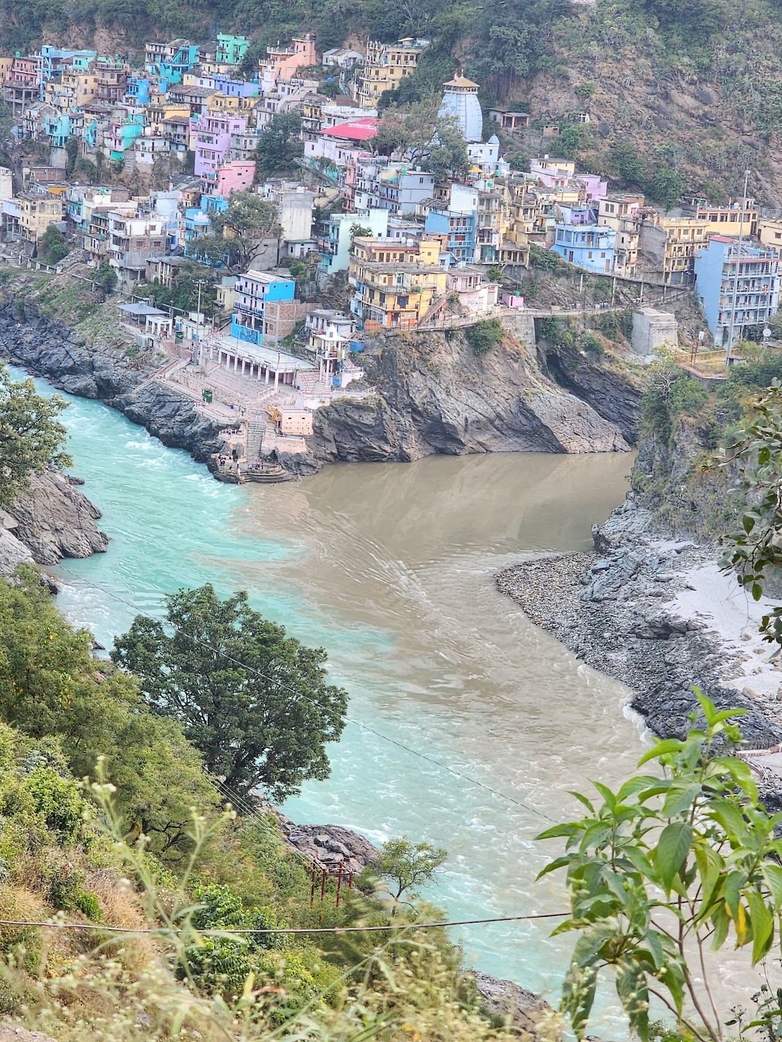 The green Bhagirathi and the brown Alaknanda meeting at Devprayag beneath a hillside town